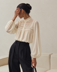 Ivory Sheer Poet Blouse with ruffled stand collar, pintucked yoke and balloon sleeves, tucked into black pleated trousers