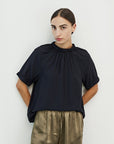 Mason Smocked Neck Blouse in black, front view with smocked mock neck and puff sleeves, worn with olive satin pants