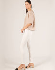 Side view of the taupe Hazel Overlap Back Top with white skinny jeans and two-tone slingback heels