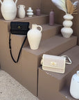 Oceans End Giovanni crossbody bags in creme and black displayed on stone steps with ceramic vases