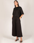 Full-length view of the black Hazel Overlap Back Top with cropped wide-leg pants and black sandals