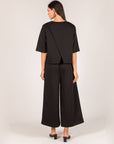 Back view of the black P.CILL Hazel Overlap Back Top with split back and wide-leg pants