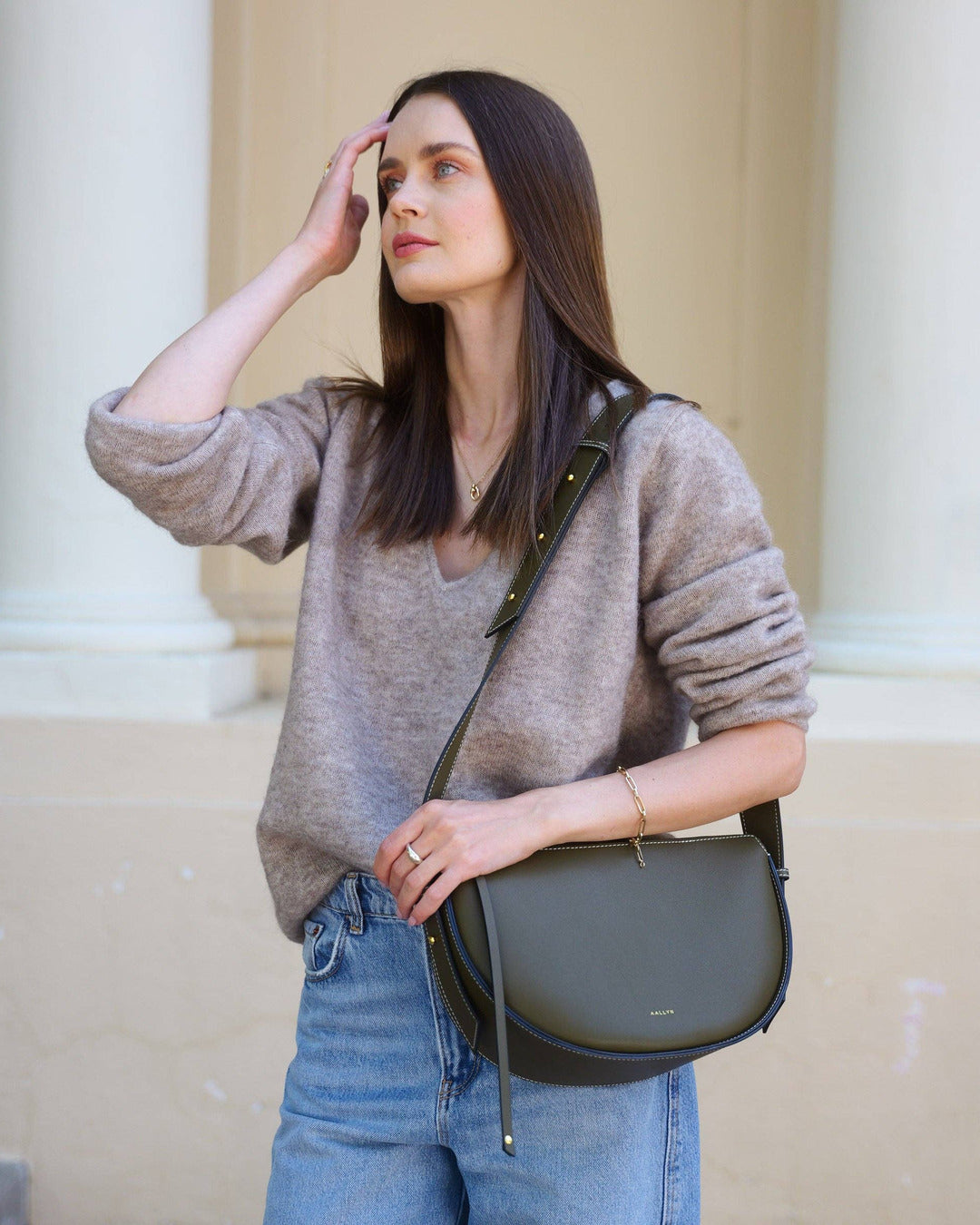 Model in a taupe sweater and jeans wearing the olive Elara bag crossbody