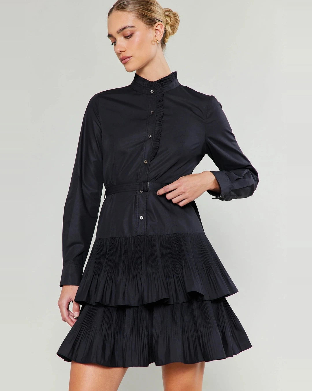 Model in the black Current Air Anberlin Mini Dress with ruffle stand collar, belted waist and tiered pleated skirt, front view