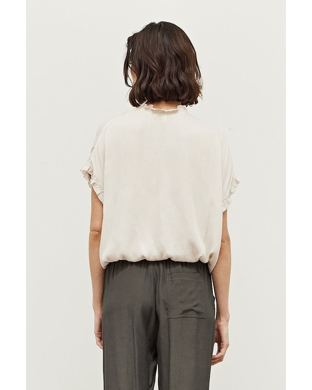 Back view of the ivory Sadie Satin Blouse with ruffle neckline and gathered elastic hem