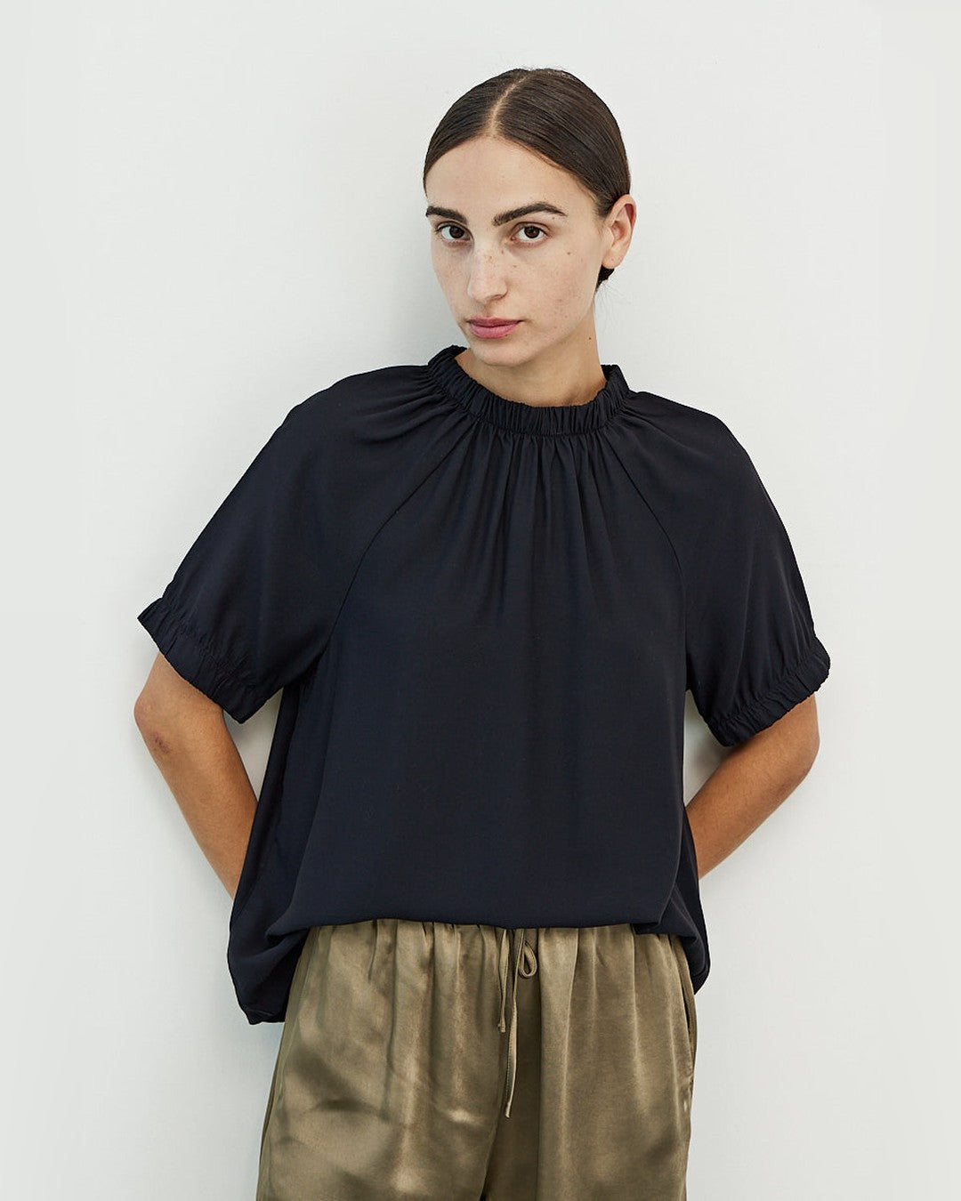 Mason Smocked Neck Blouse in black, front view with smocked mock neck and puff sleeves, worn with olive satin pants