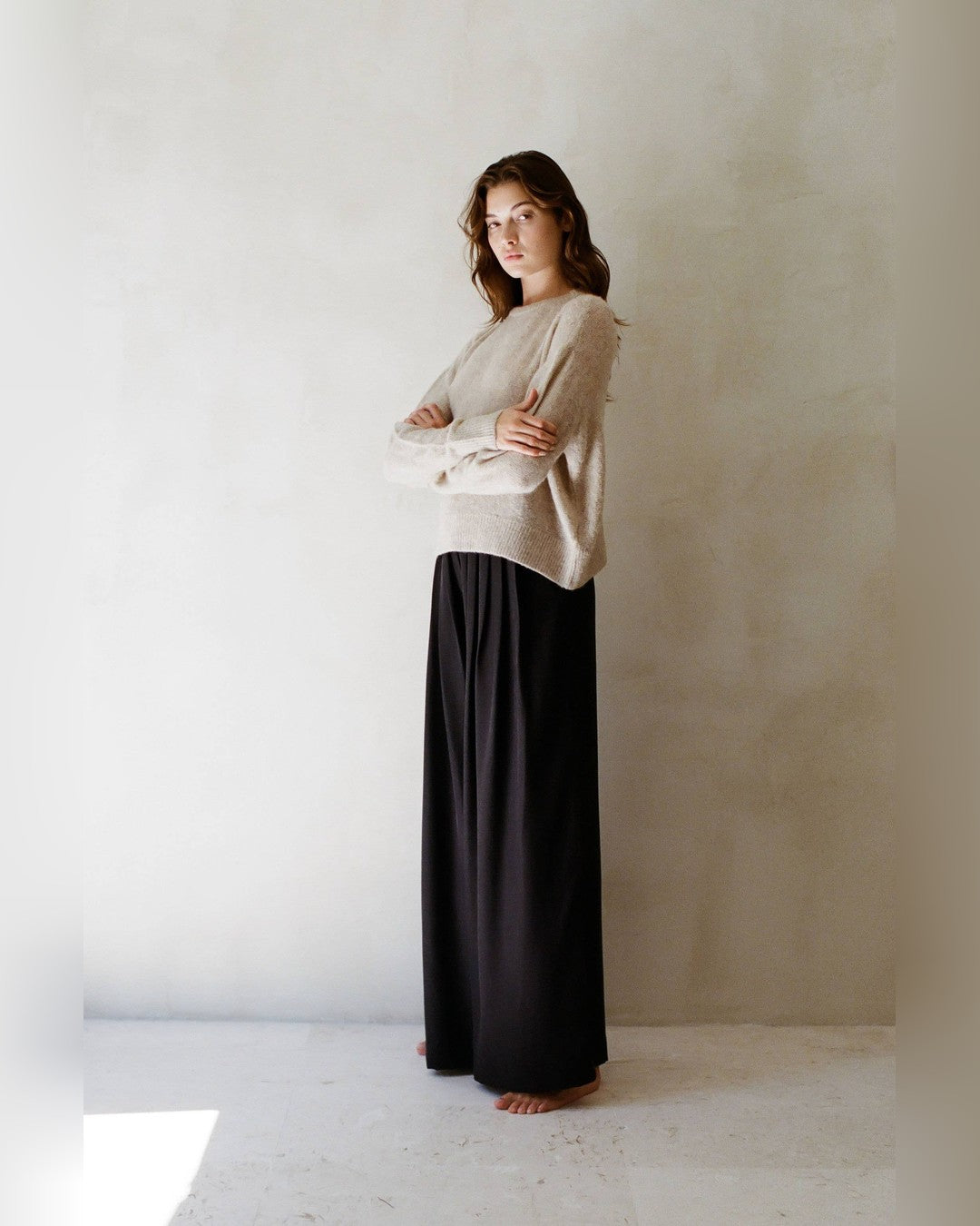 Beige Evie crew neck sweater with ribbed cuffs, styled with black wide-leg trousers, three-quarter view