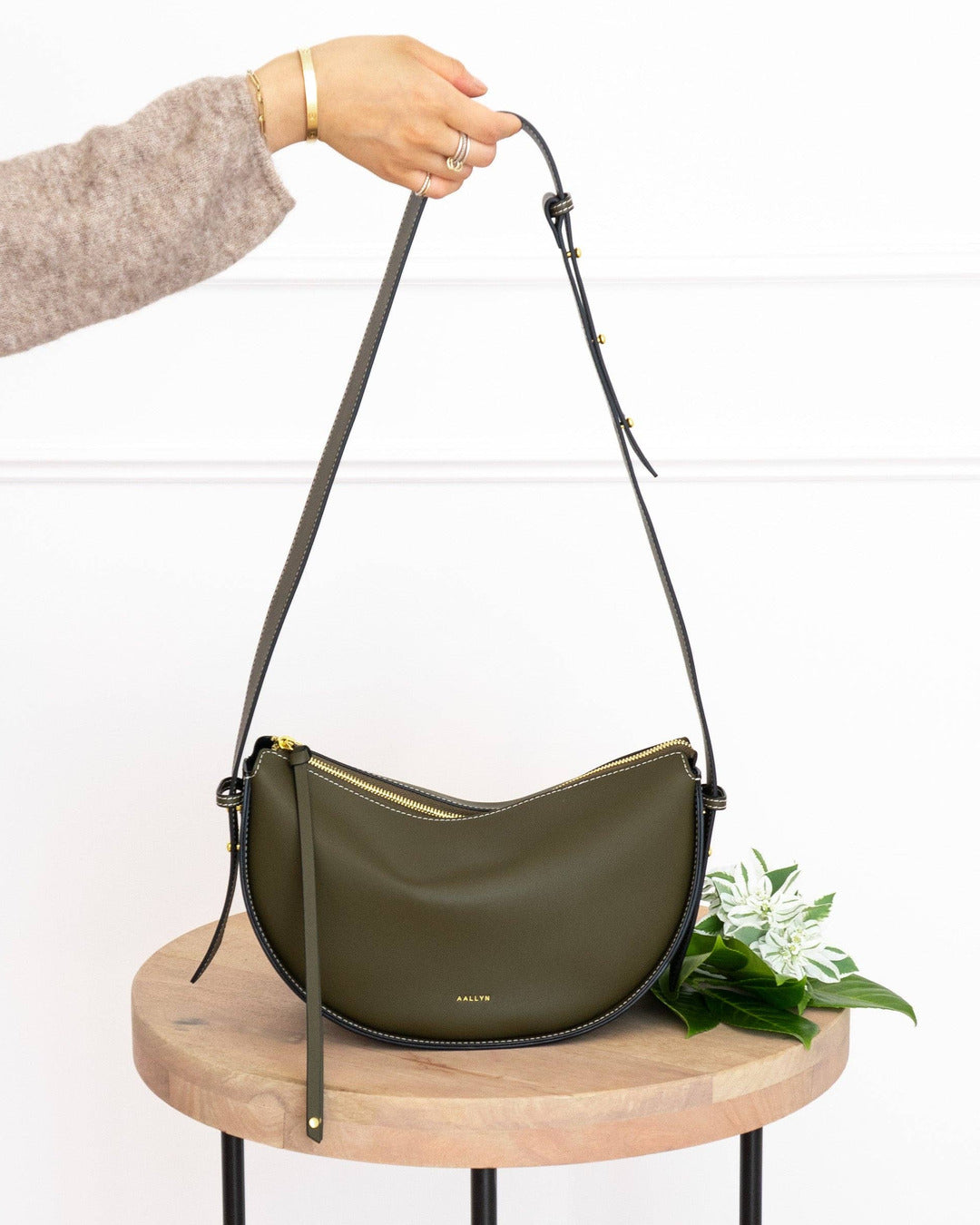 Olive Elara bag with gold zip hanging from its long adjustable shoulder strap above a wooden table