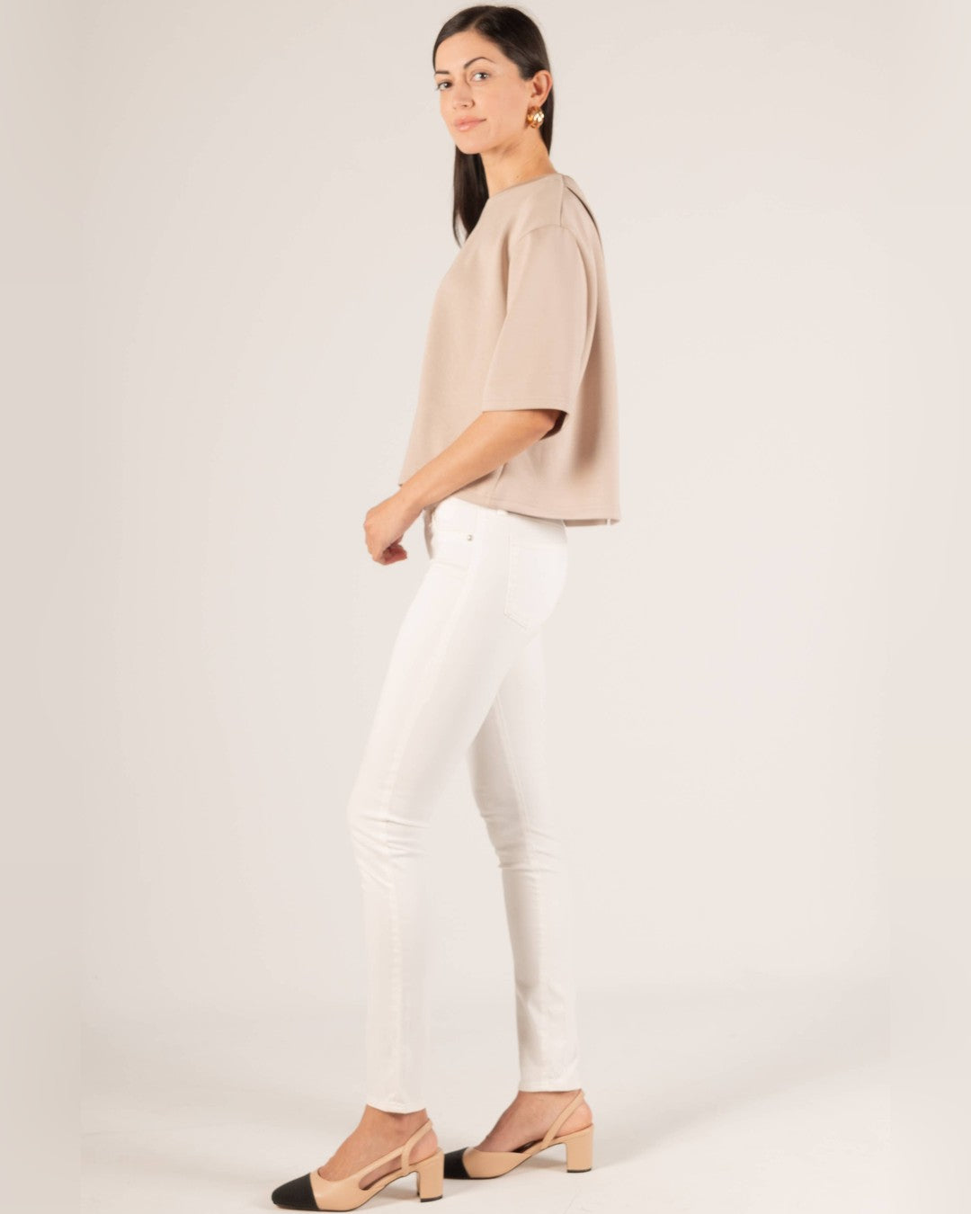 Side view of the taupe Hazel Overlap Back Top with white skinny jeans and two-tone slingback heels