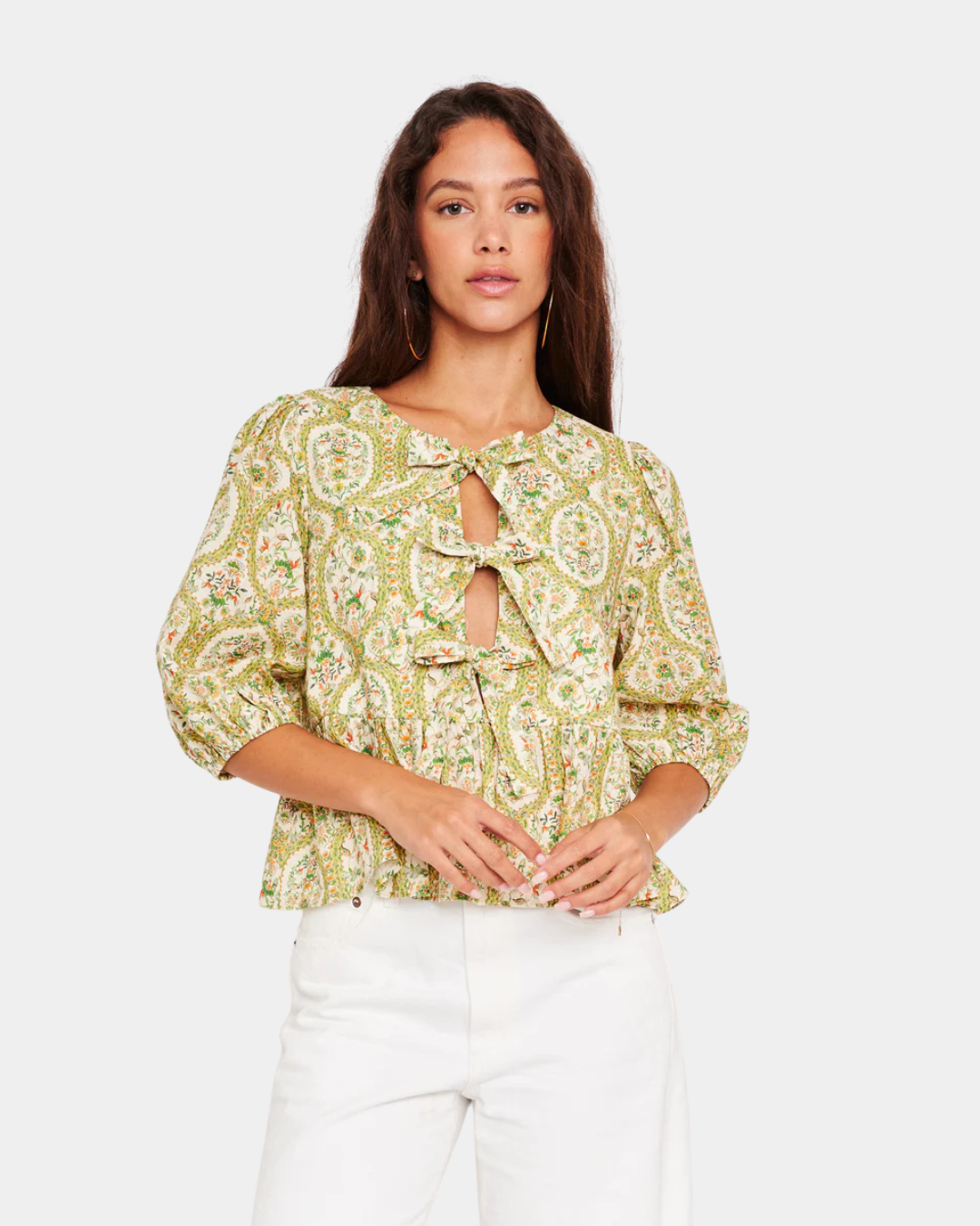 Model wearing D.RA Ros floral bow front top with puff sleeves and peplum silhouette in green and yellow print.