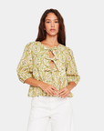 Model wearing D.RA Ros floral bow front top with puff sleeves and peplum silhouette in green and yellow print.