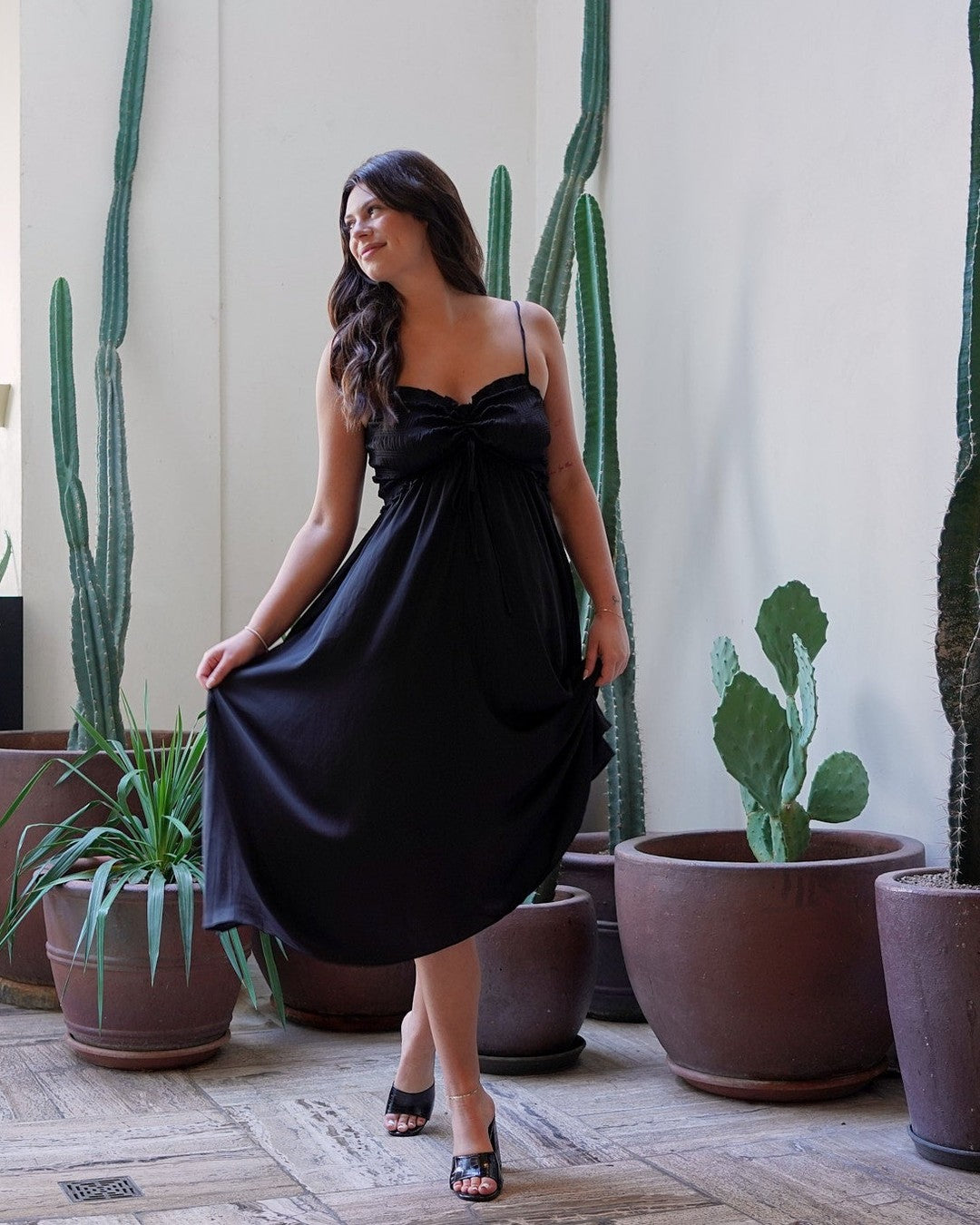 Model holding the skirt of the black Prescott Midi Dress on a patio with potted cacti