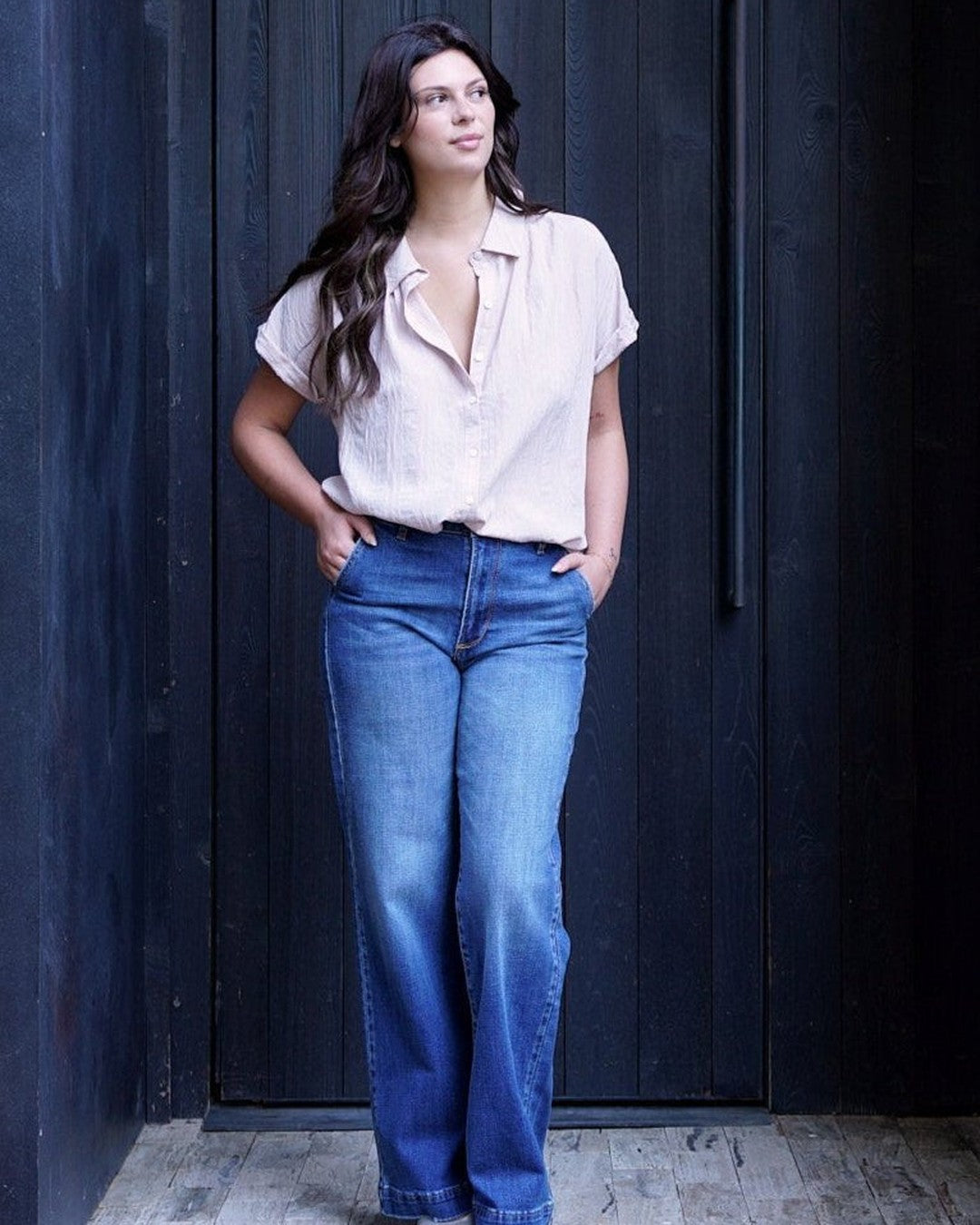 Model in KanCan medium-wash denim trousers with a blush short-sleeve button-up