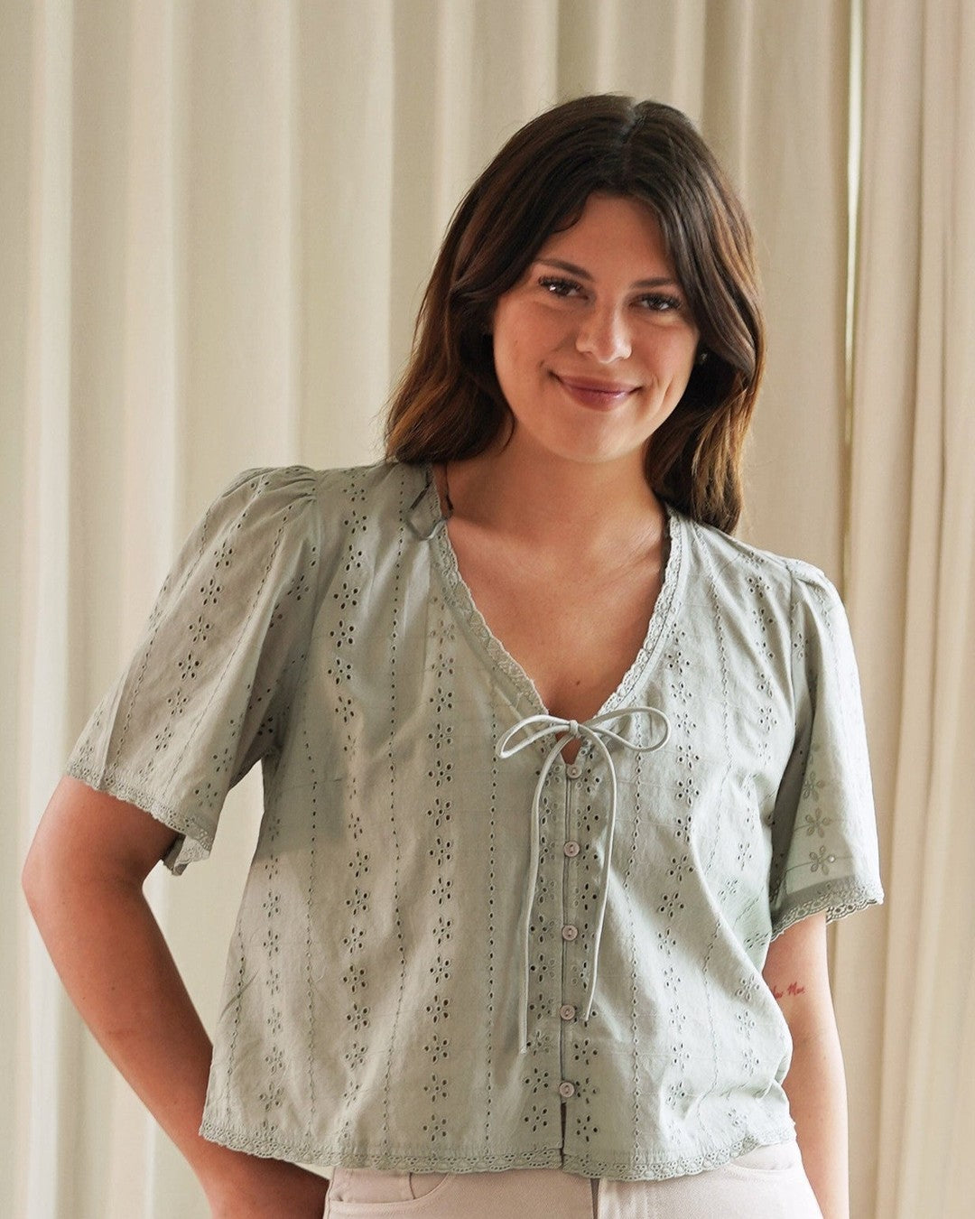 Smiling model in the sage green Jessa cotton eyelet blouse with cream jeans, front view