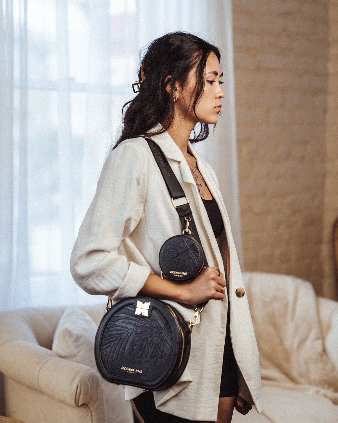 Model in a cream cardigan wearing a round black Oceans End crossbody on the black Luxe Strap