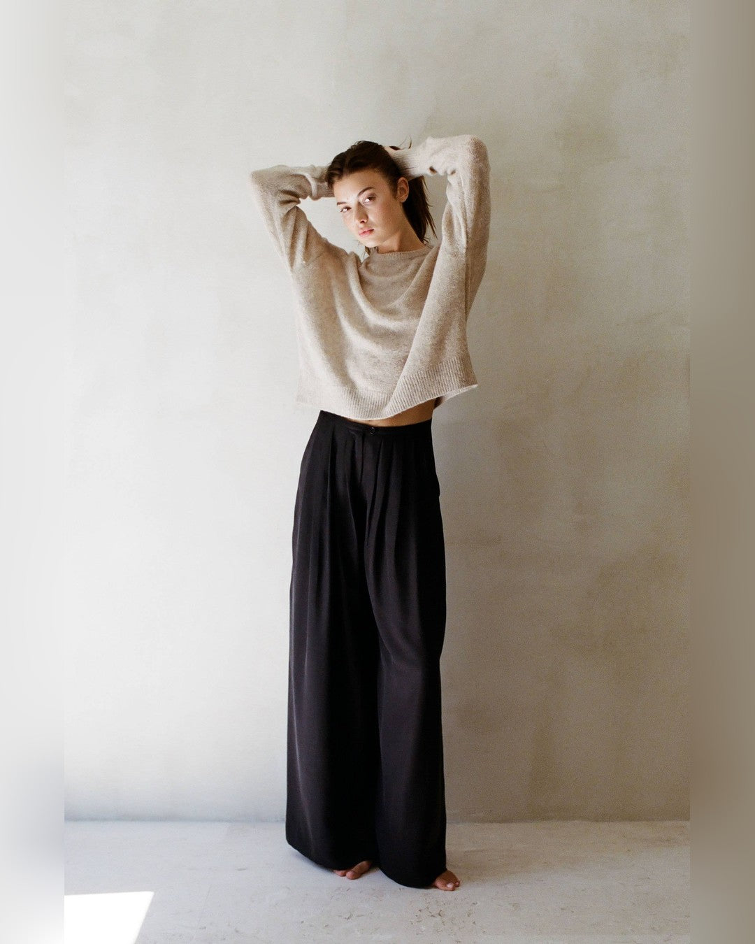 Full-length view of the beige Evie Pullover Sweater, slightly cropped over black pleated wide-leg trousers