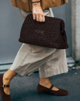 Model in cream trousers and burgundy Mary Janes carrying the Daniella Lehavi Vivian Maxi Clutch in chocolate by hand