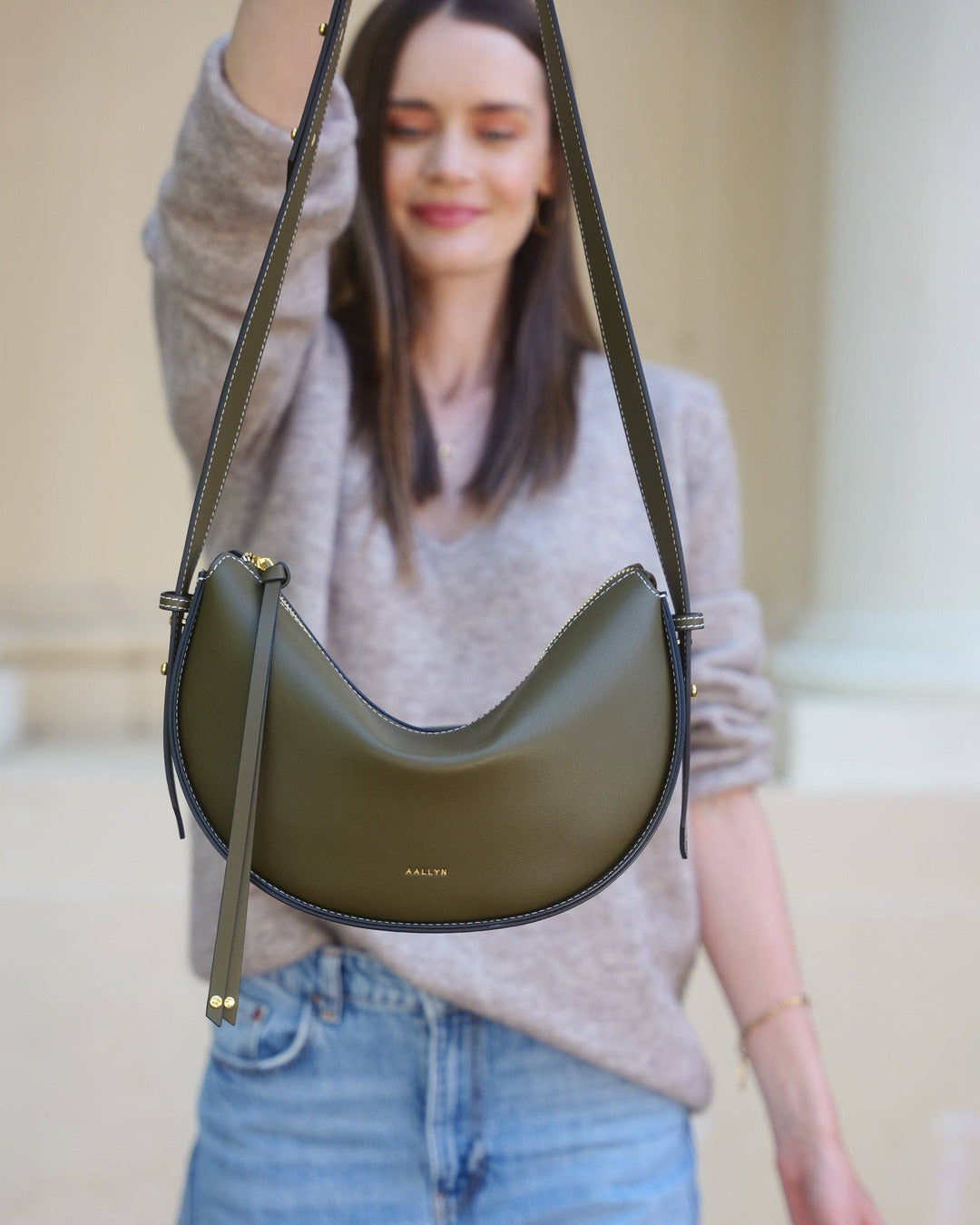 Model holding the olive Elara bag out in front by its shoulder strap