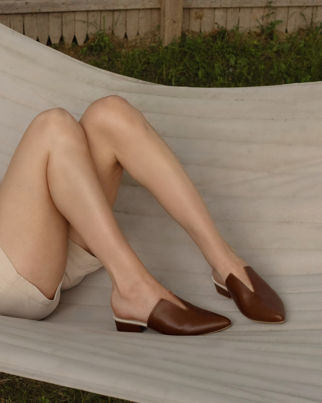 Model reclining in a hammock wearing Stivali Pijao tan leather mules with cream shorts