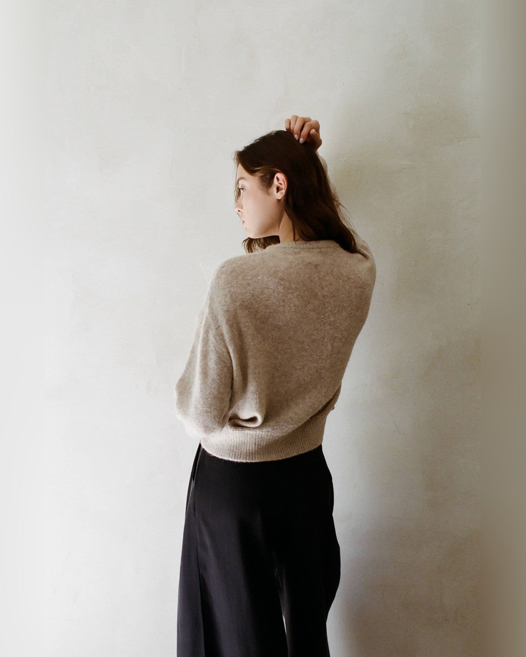 Back view of the heathered beige Evie Pullover Sweater with black wide-leg trousers