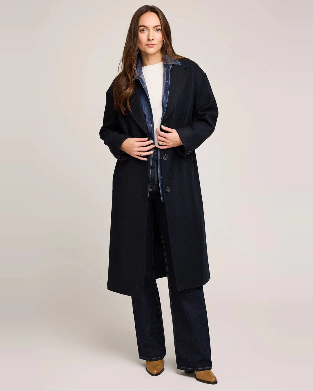 Model in the long navy Gentle Fawn Agatha Coat over a denim shirt, white tee and dark wide-leg jeans with tan boots