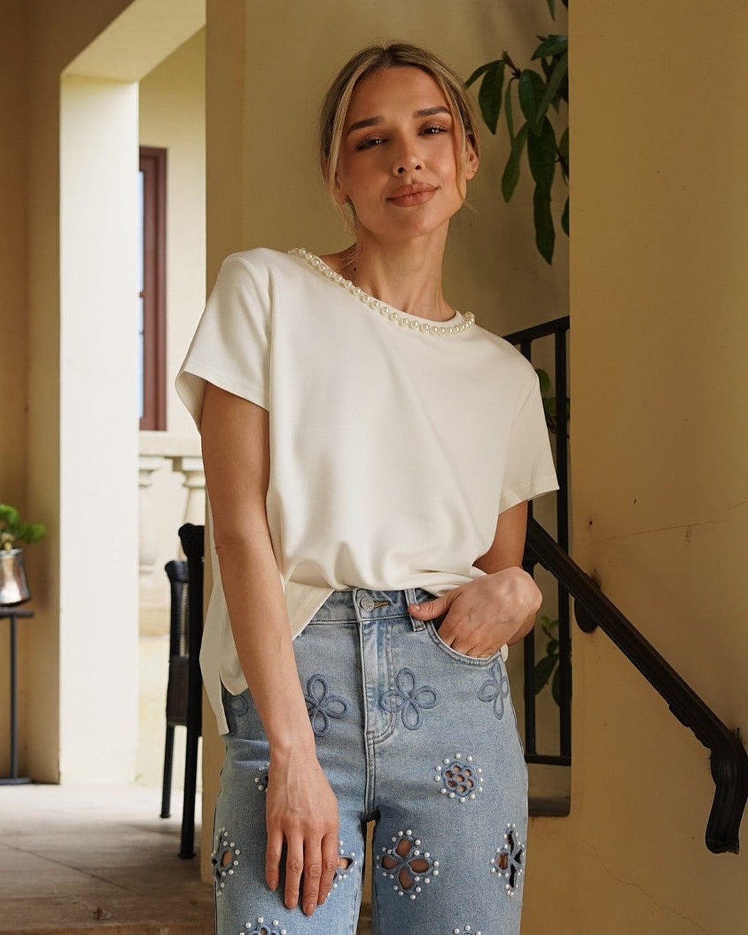 Ivory Monaco Pearl Trim Tee tucked into embellished light wash jeans on a sunny terrace