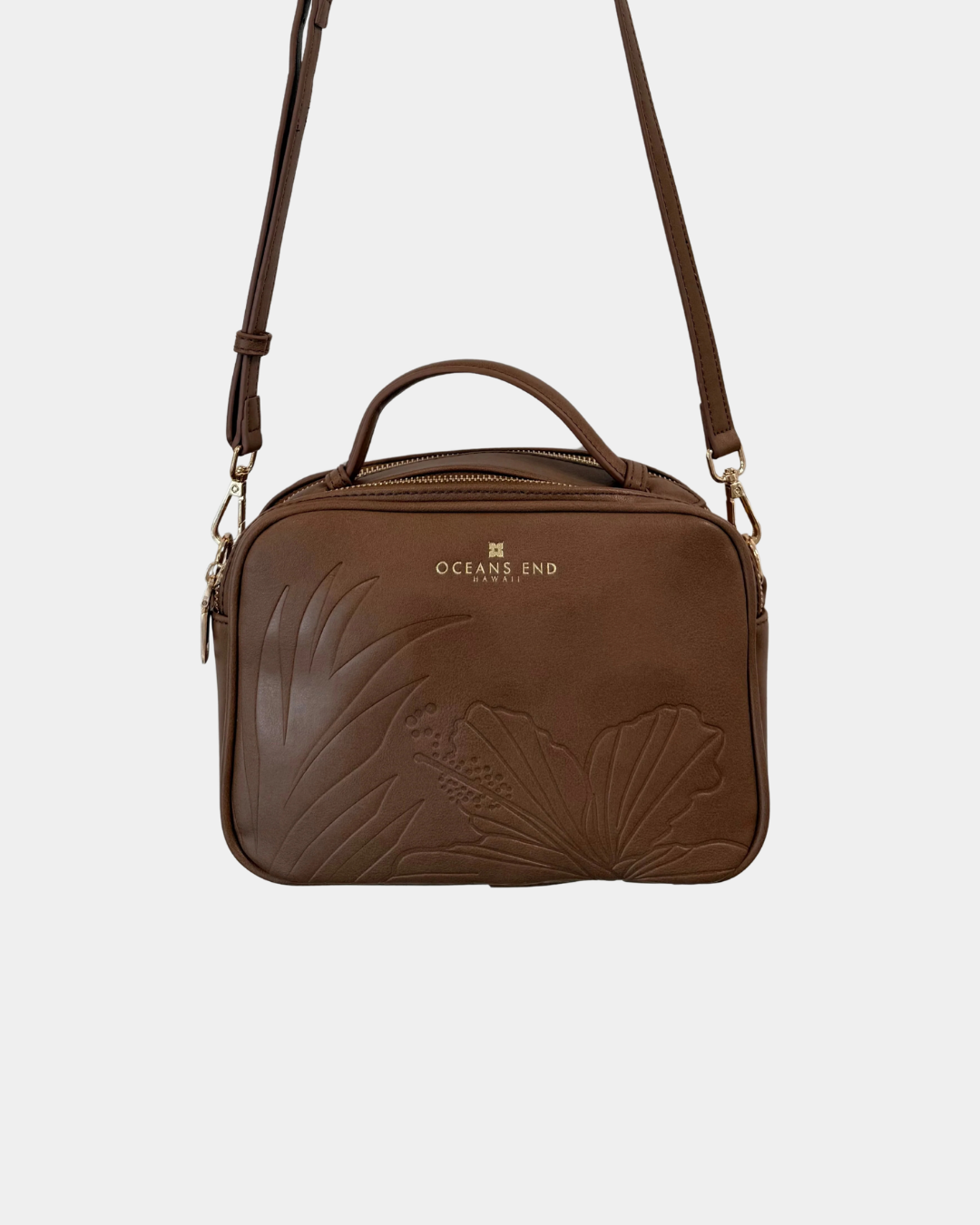 Oceans End Justine 2.0 crossbody bag in mocha featuring an embossed hibiscus design, top handle, adjustable crossbody strap, and gold-tone hardware.