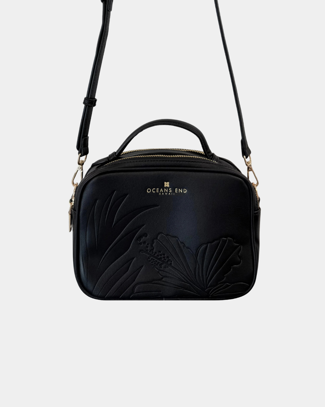 Oceans End Justine 2.0 crossbody bag in onyx featuring an embossed hibiscus design, top handle, adjustable crossbody strap, and gold-tone hardware.