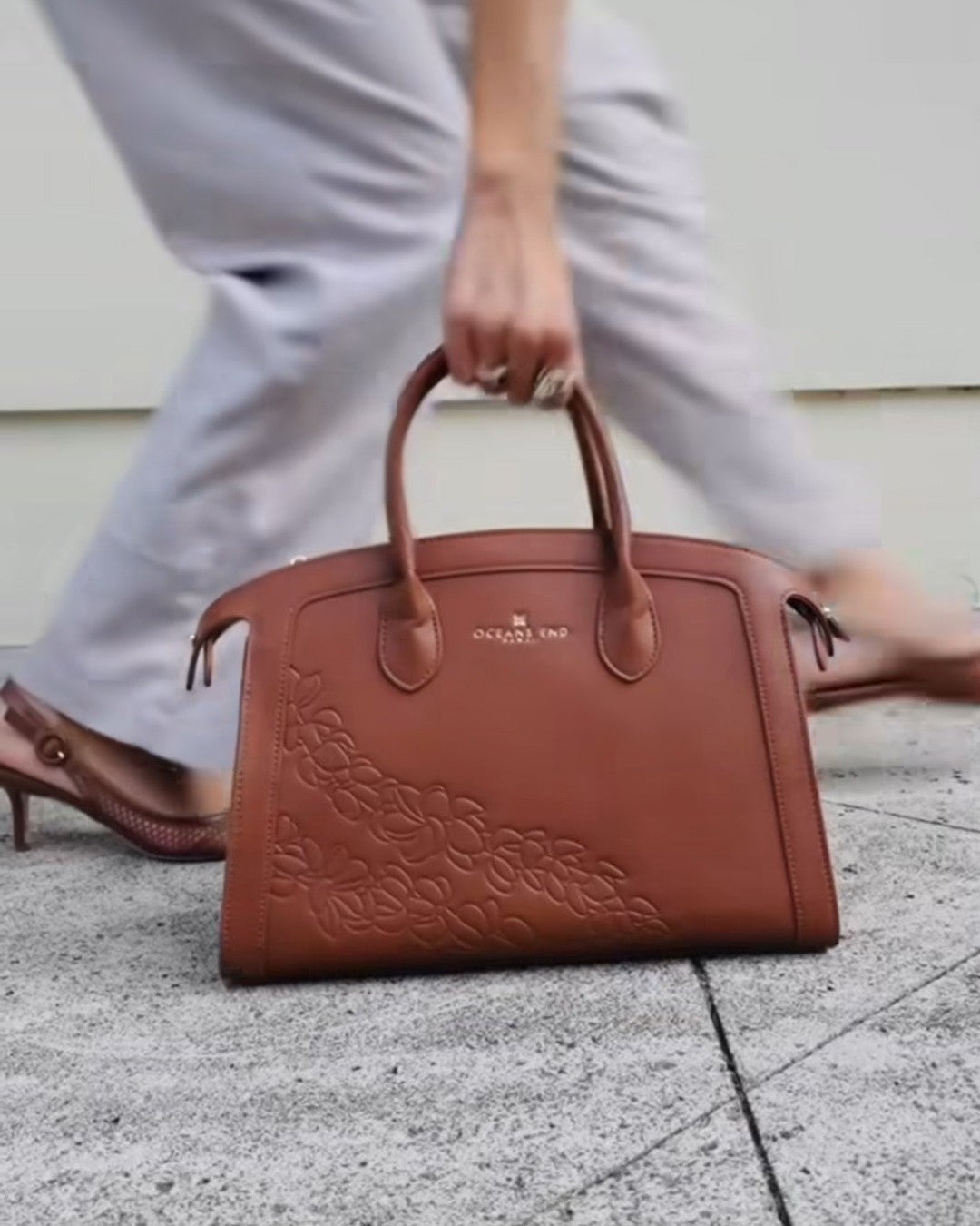 Model carrying the Oceans End Leialoha saddle handbag by its top handles