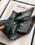 Close-up detail of the Painted Totems mulberry silk scarf showing the colorful totem artwork and smooth luxury silk texture.