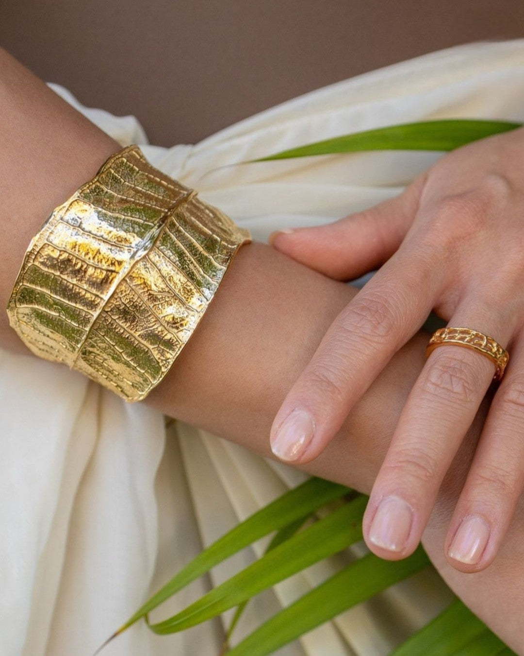 Gold Plumeria Cuff Bracelet and Thin Coral Band Ring worn with a cream wrap and palm leaves