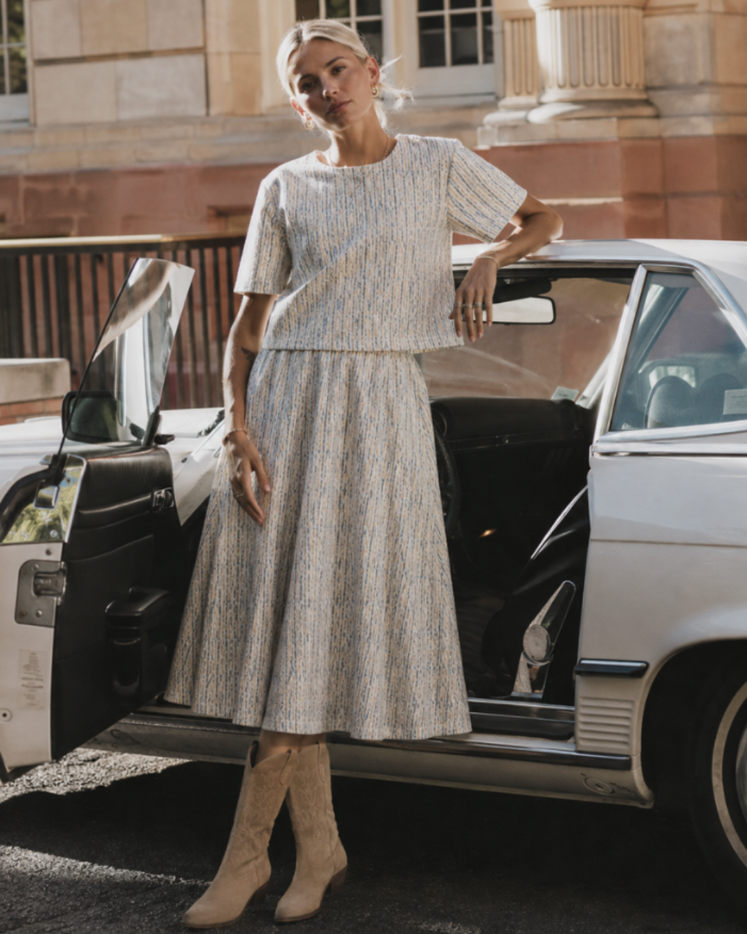 Azure Horizon Top and matching midi skirt in ivory and blue textured stripe, worn with tan western boots beside a white car