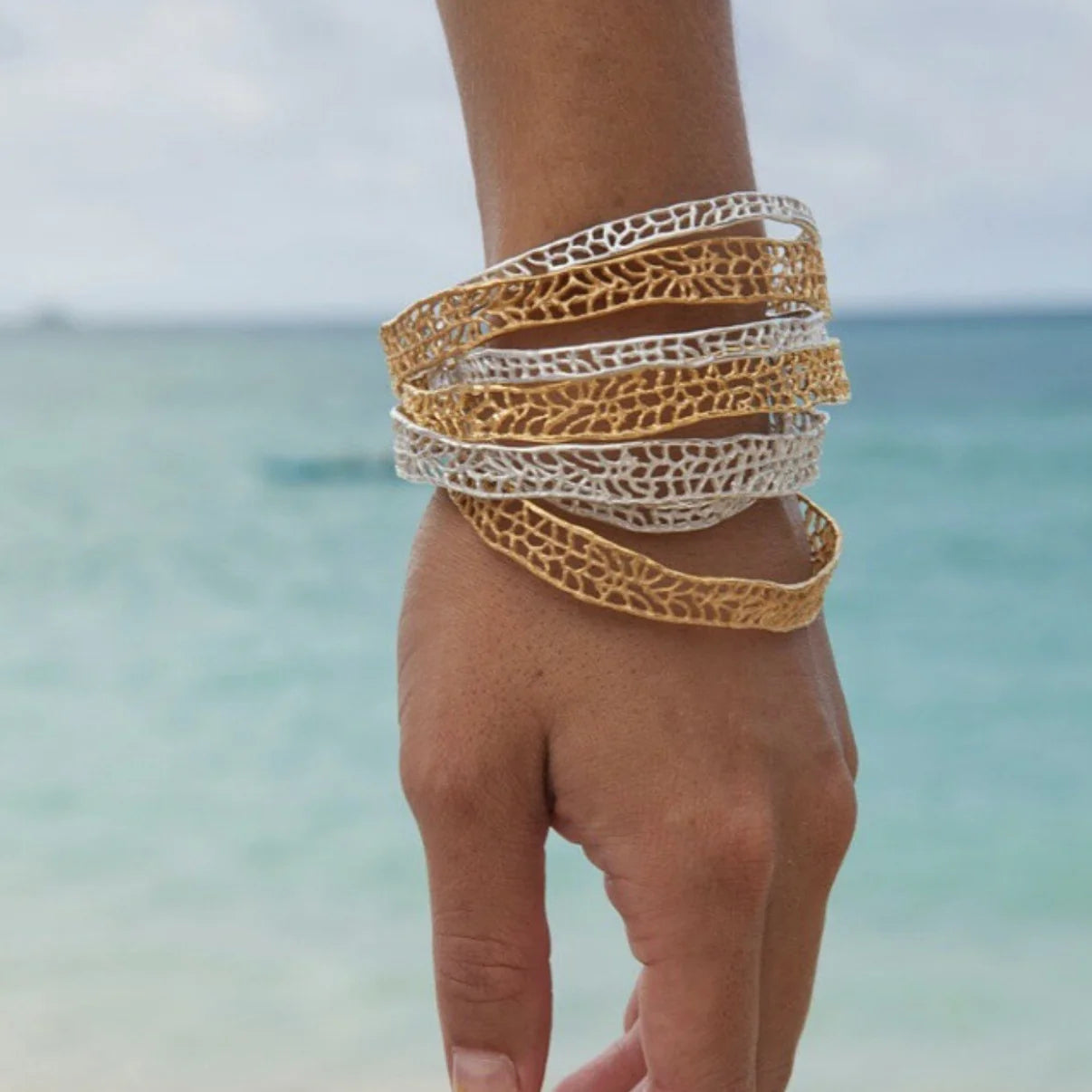 Handcrafted thin gold coral bangle bracelet with organic texture on model at beach